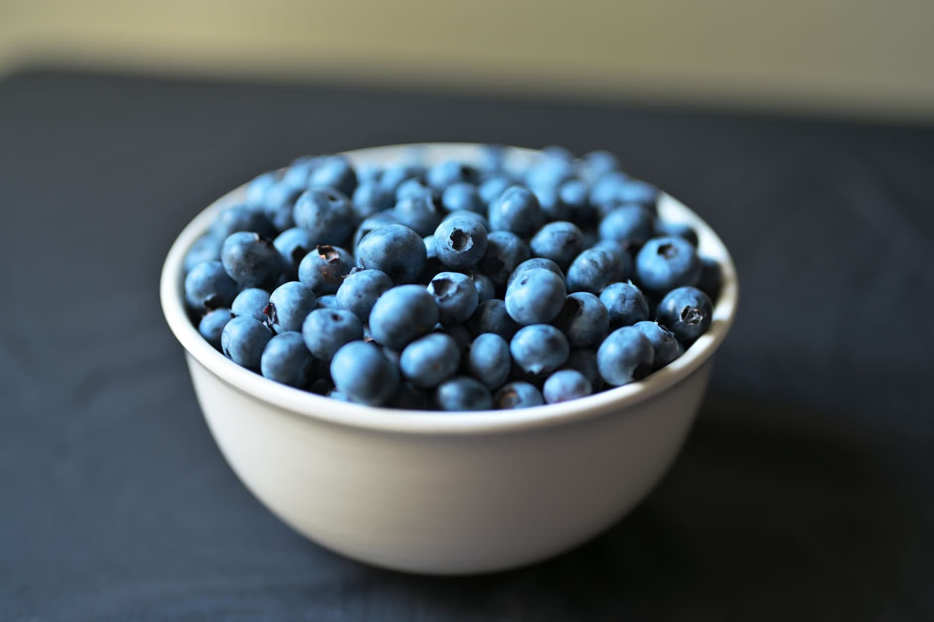 A white bowl filled with fresh, round blueberries sits on a dark surface.