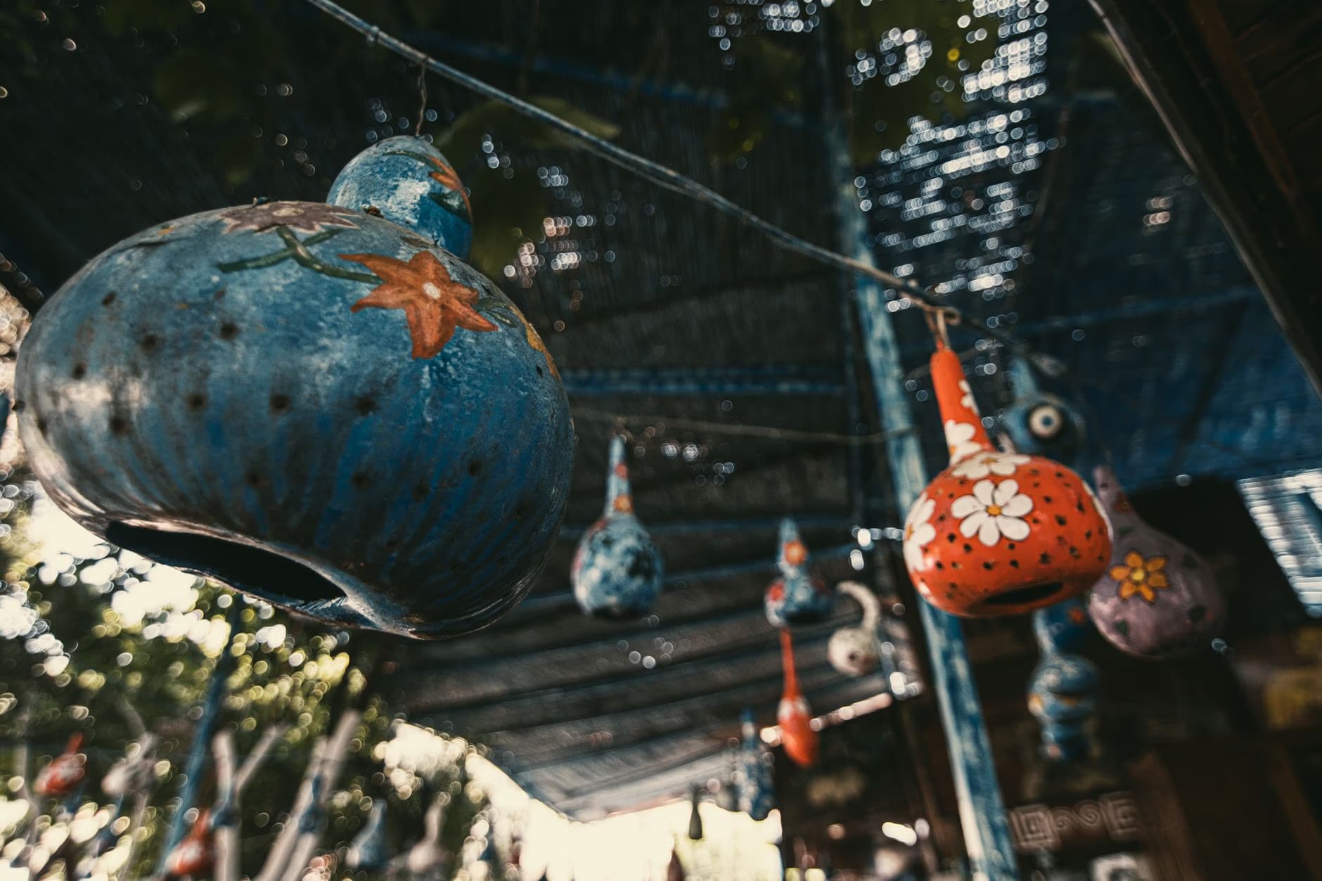 Colorful painted gourd decorations hang from a line under a shaded outdoor structure.
