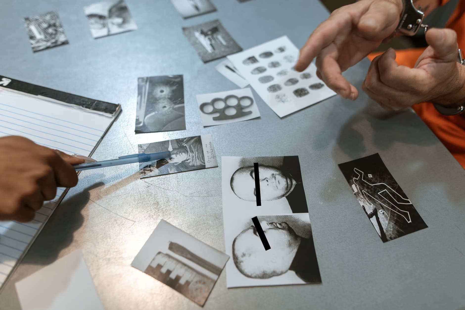 Hands examine various black-and-white crime scene photos on a table with handcuffs.
