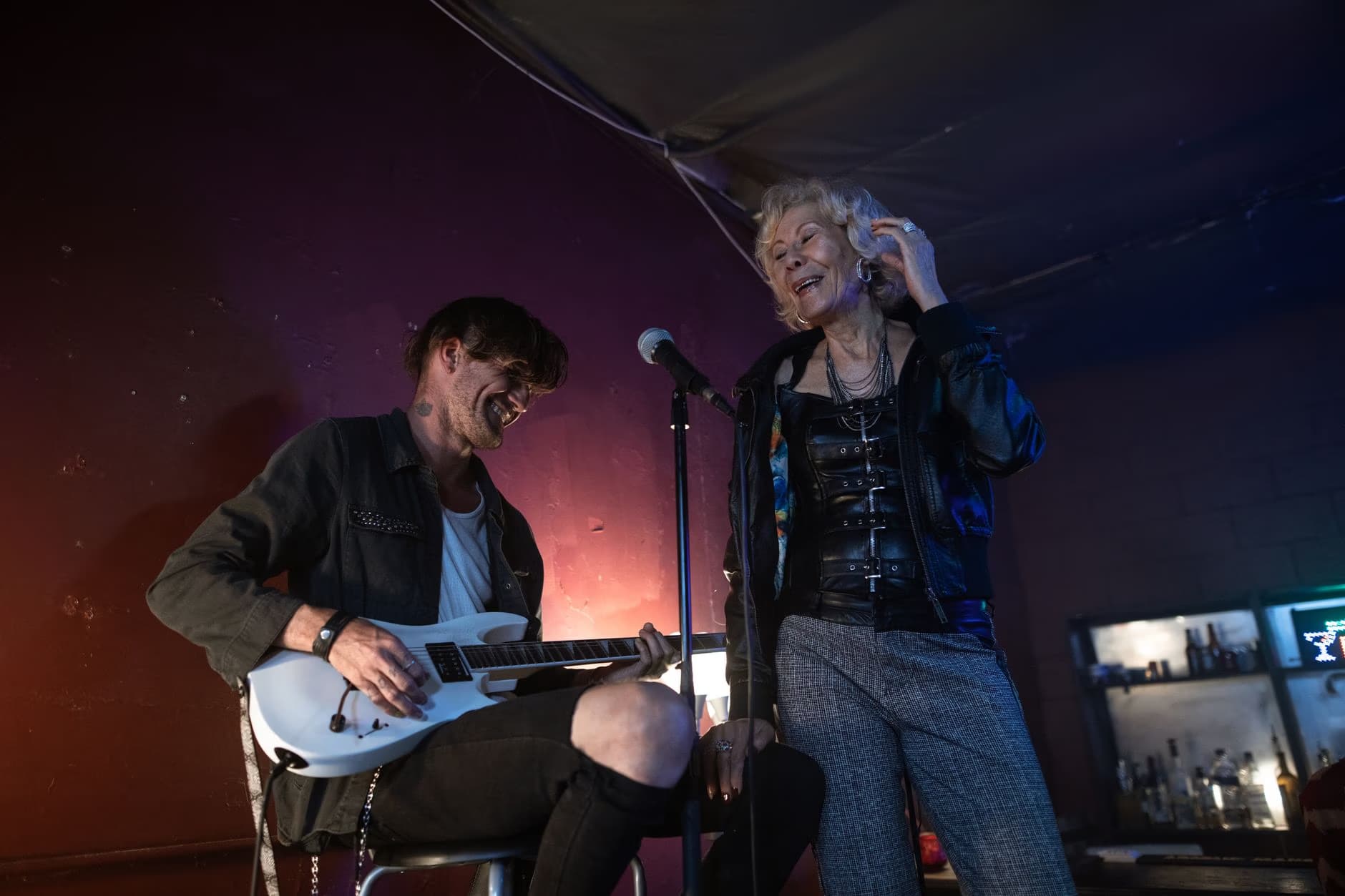 A man plays guitar while a woman sings into a microphone on a stage.