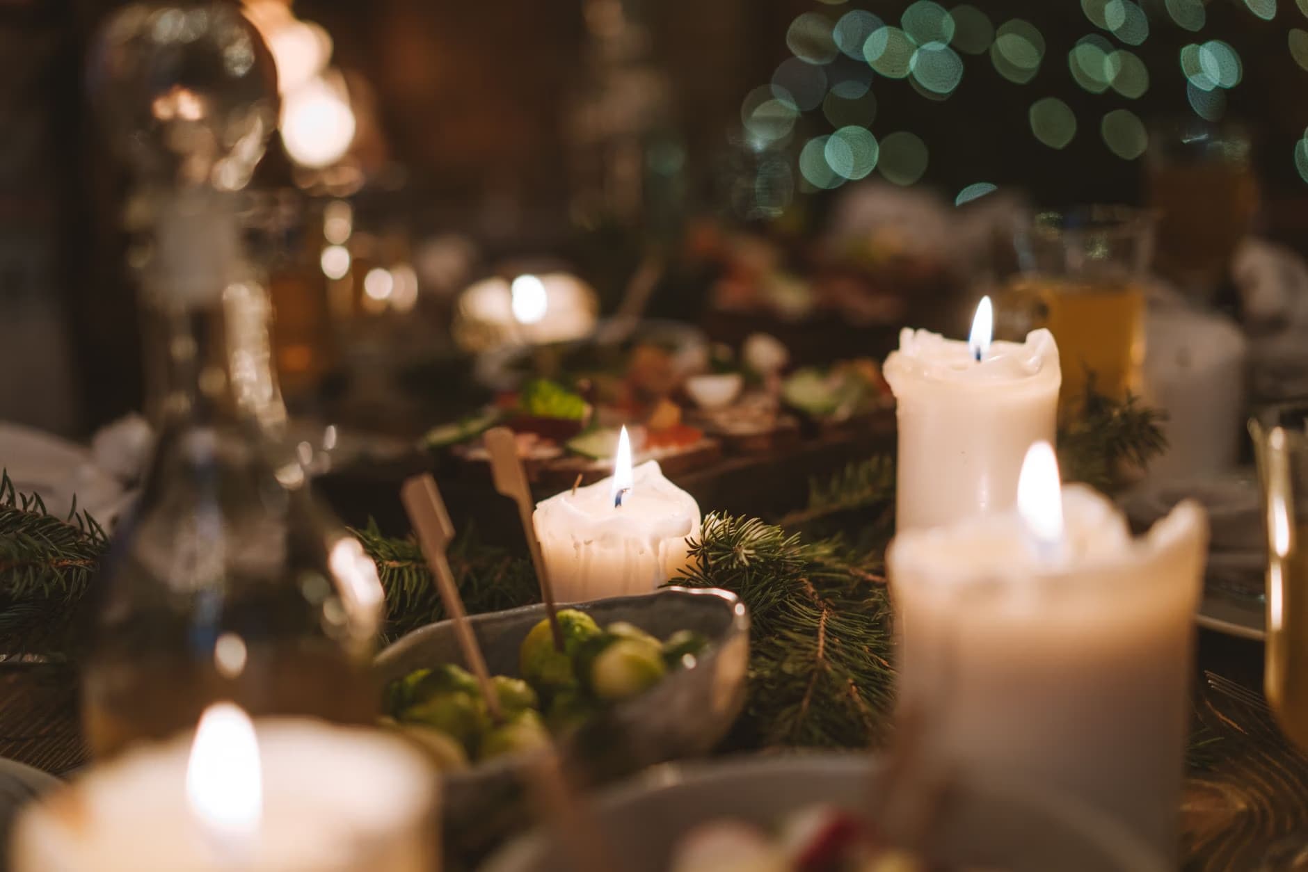 Several lit white candles illuminate a festive dining table decorated with pine branches.