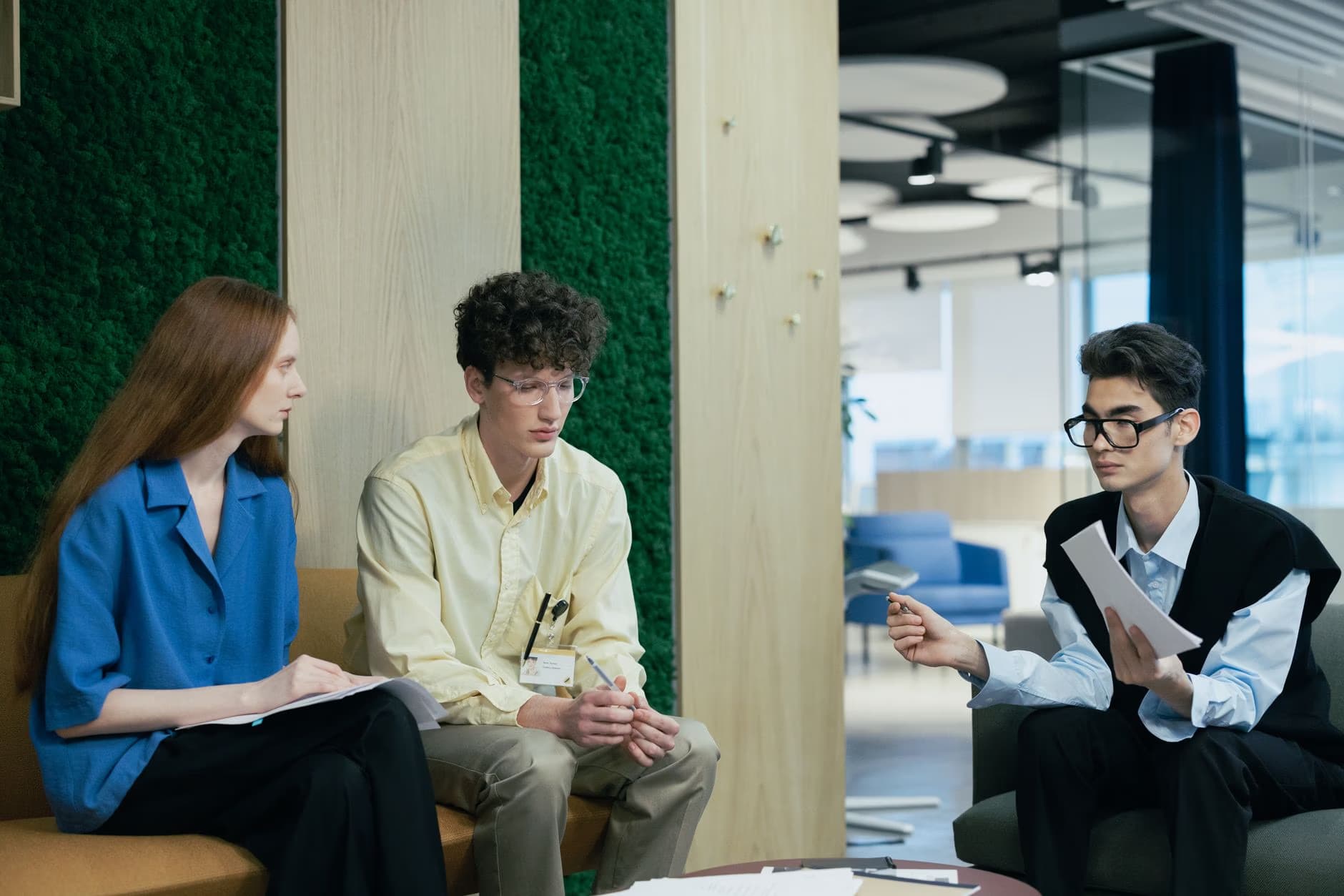 Three young office workers sit in a modern meeting area having a discussion.