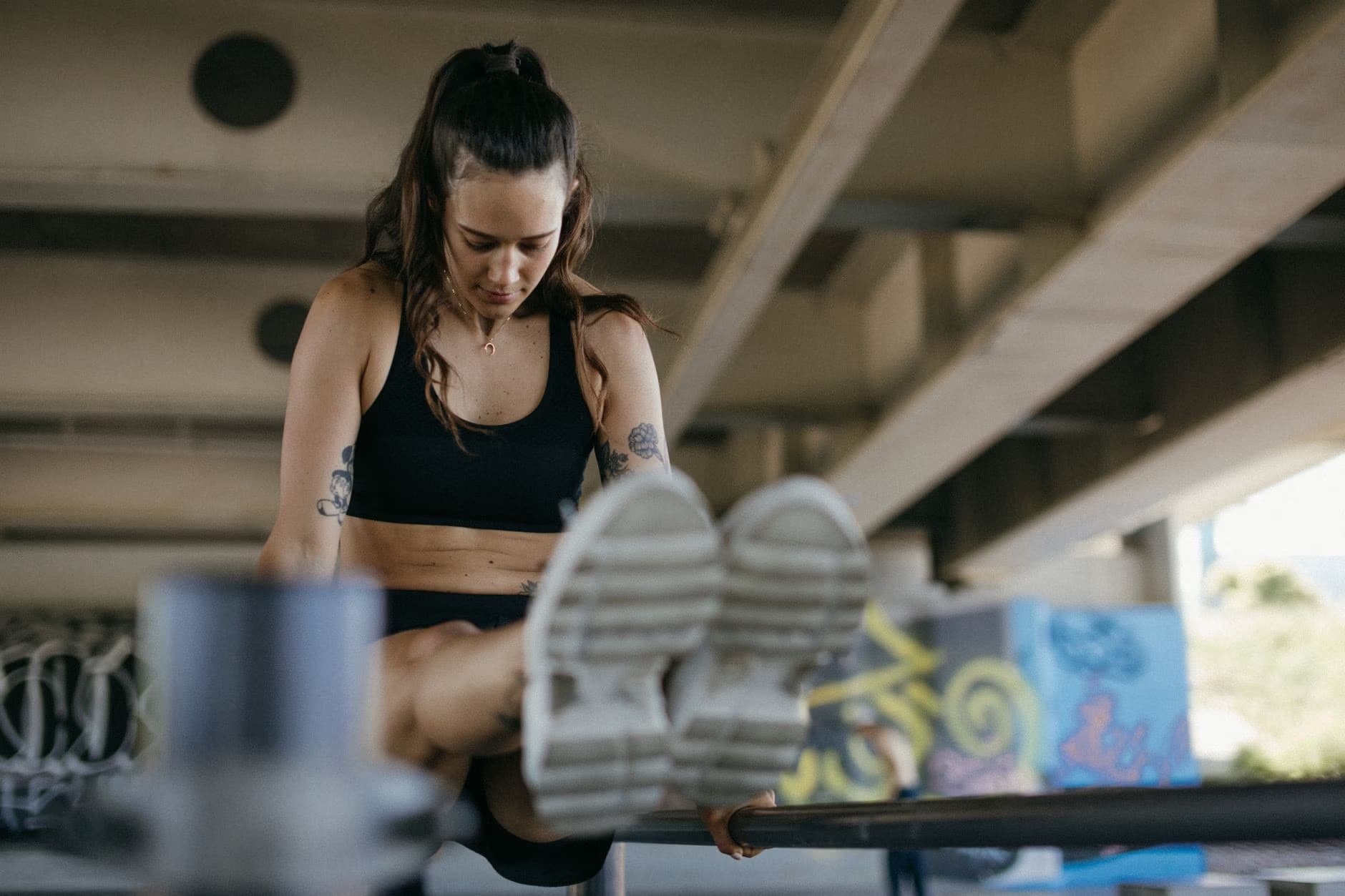 Žena ve sportovním oblečení cvičí na hrazdě v exteriéru pod betonovým mostem.