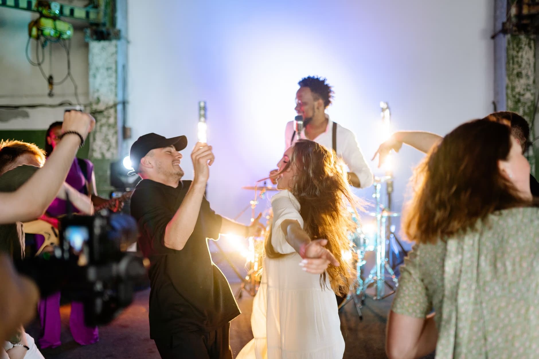 People dance at a lively party with a musician performing in the background.