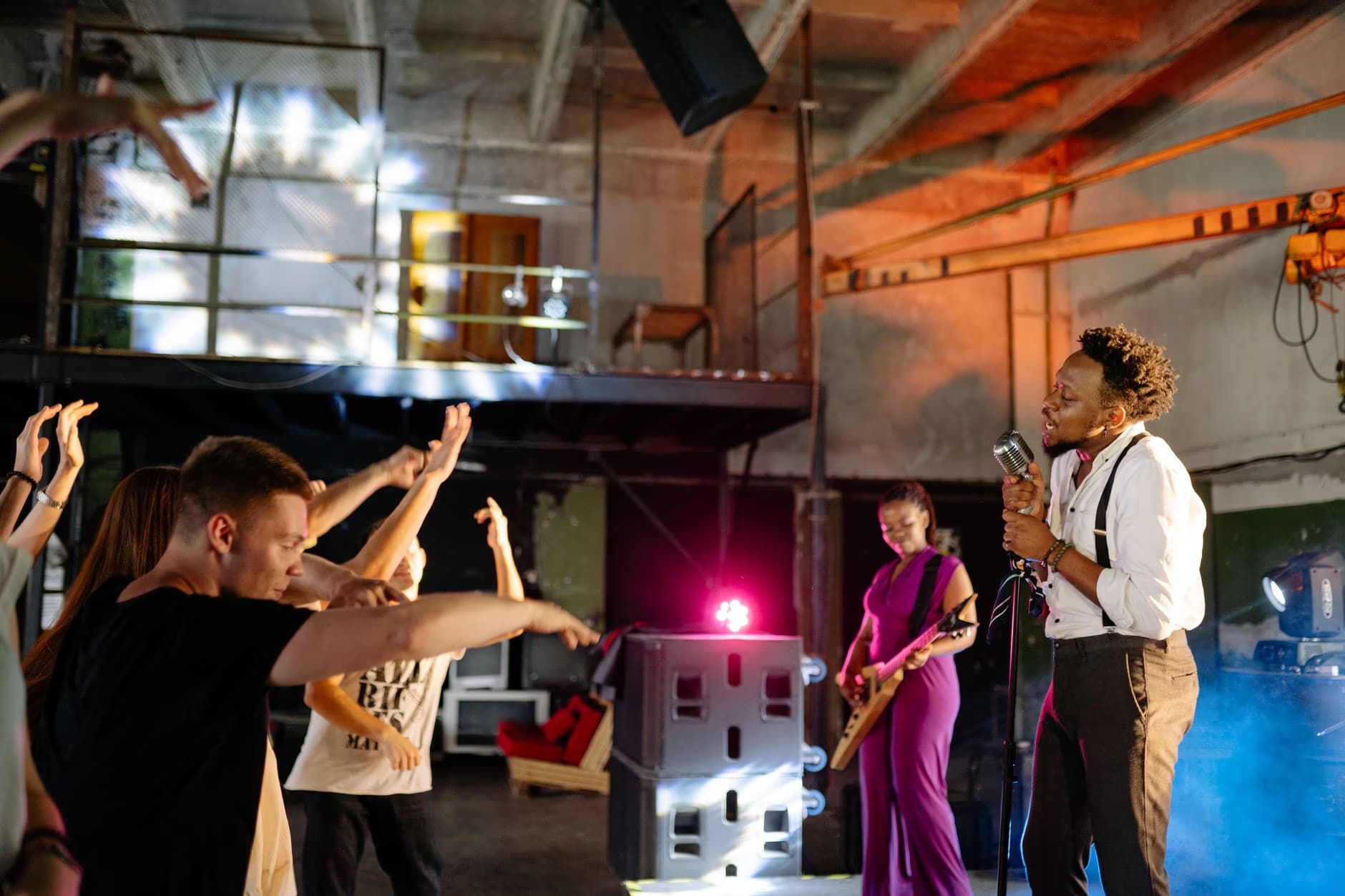 A band performs on stage for a crowd in an industrial style venue.