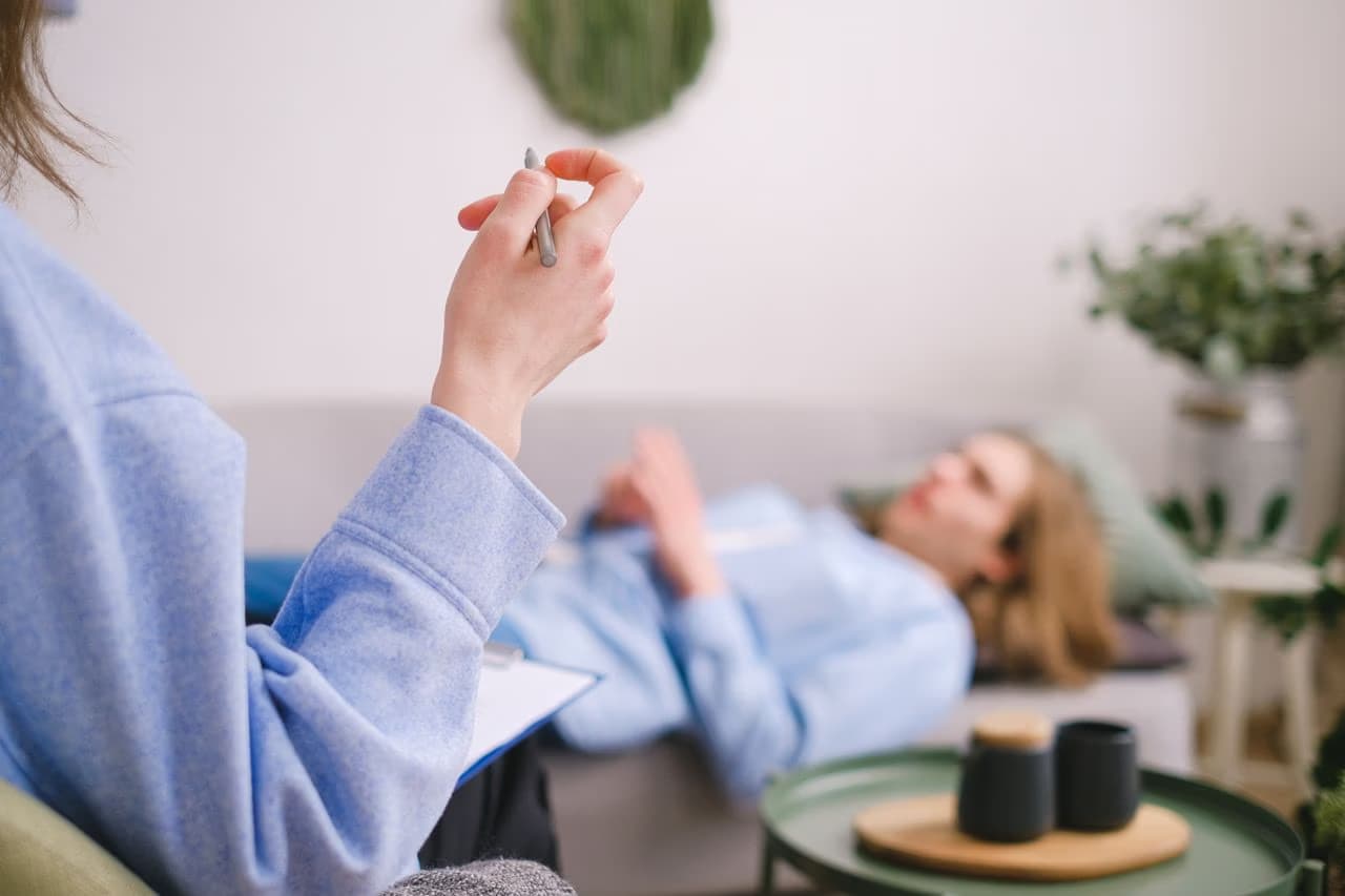 A therapist holds a pen while a client rests on a couch during a counseling session.