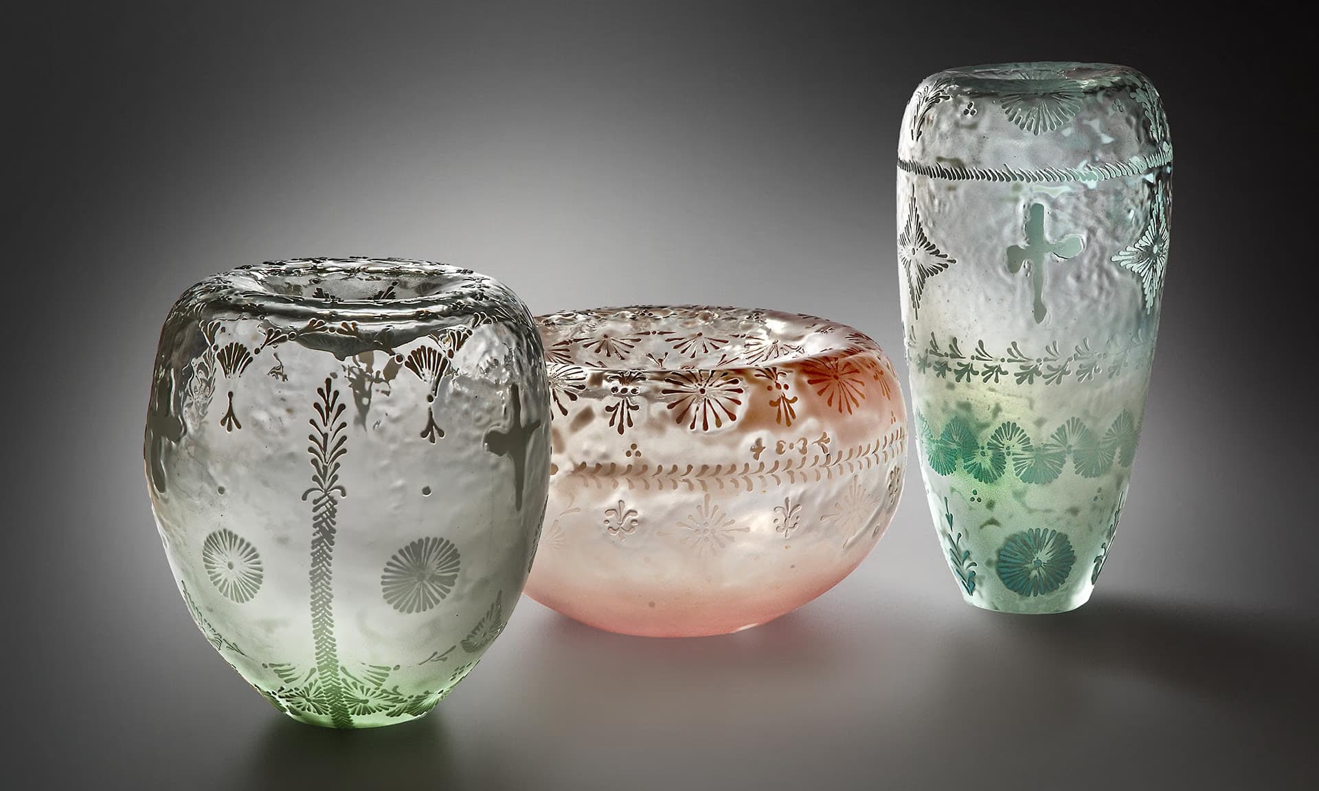 Three decorated glass vessels stand against a dark, neutral background.