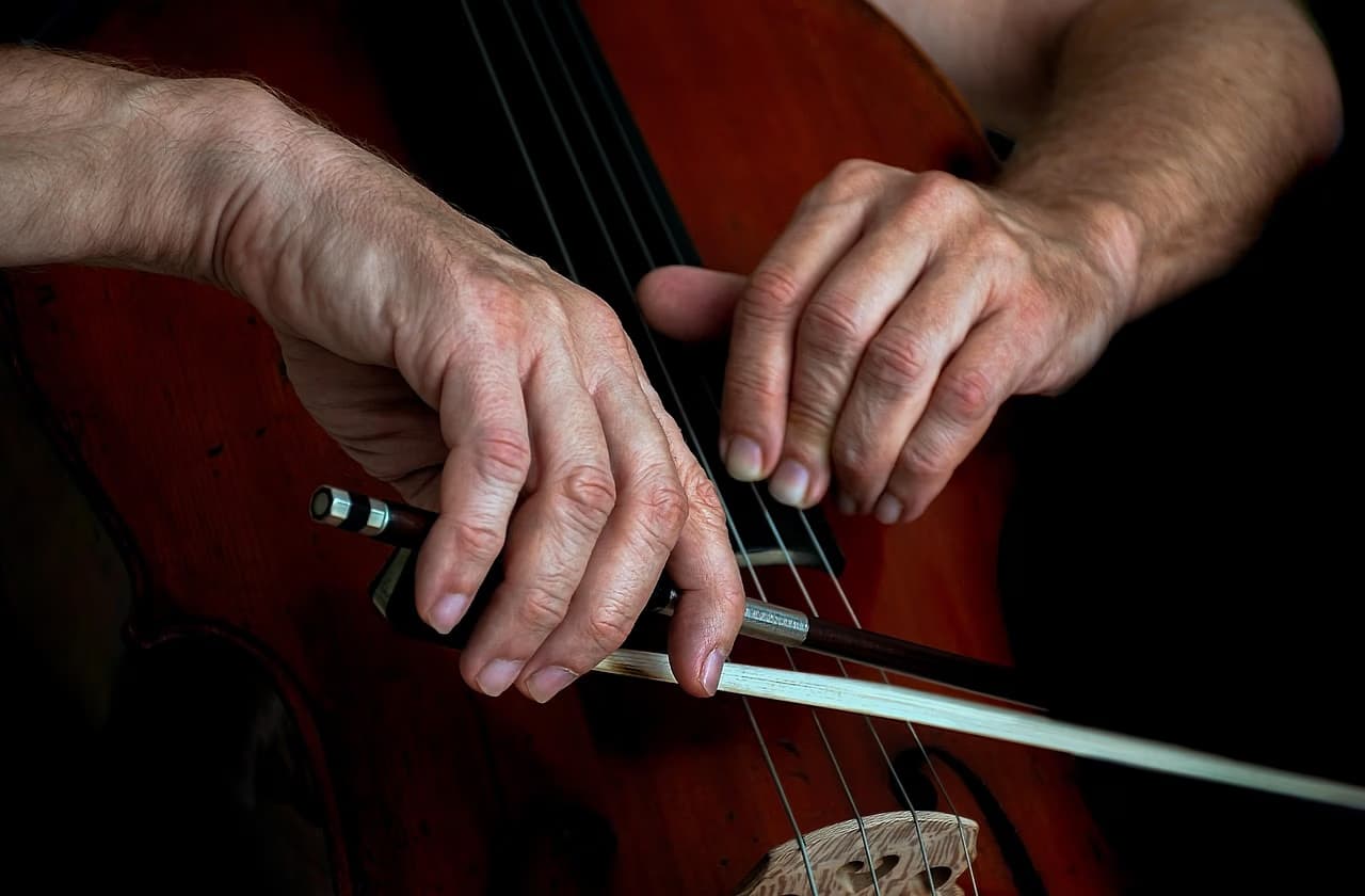 Close-up of a musician's hands playing a wooden cello against a dark background.