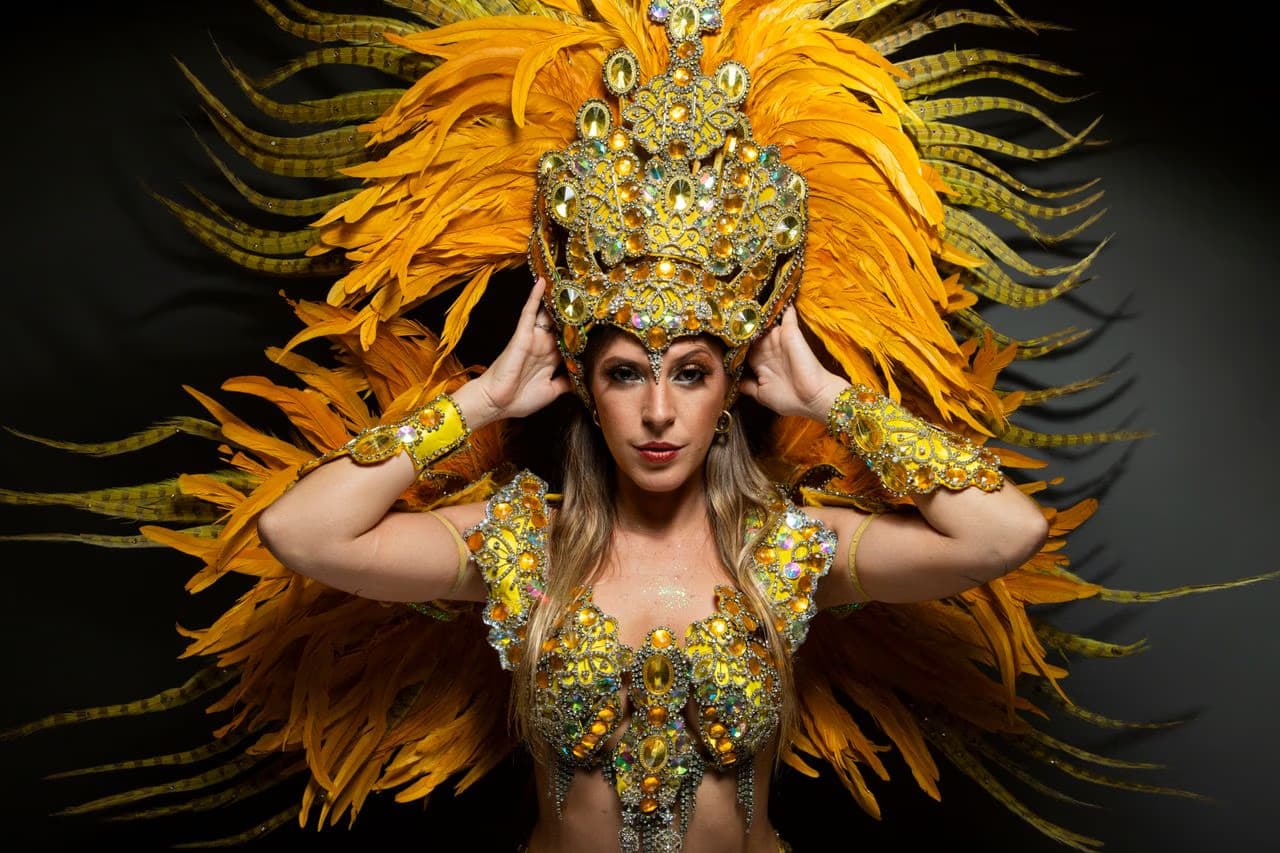 A woman wears an elaborate yellow and gold feathered carnival costume and headpiece.