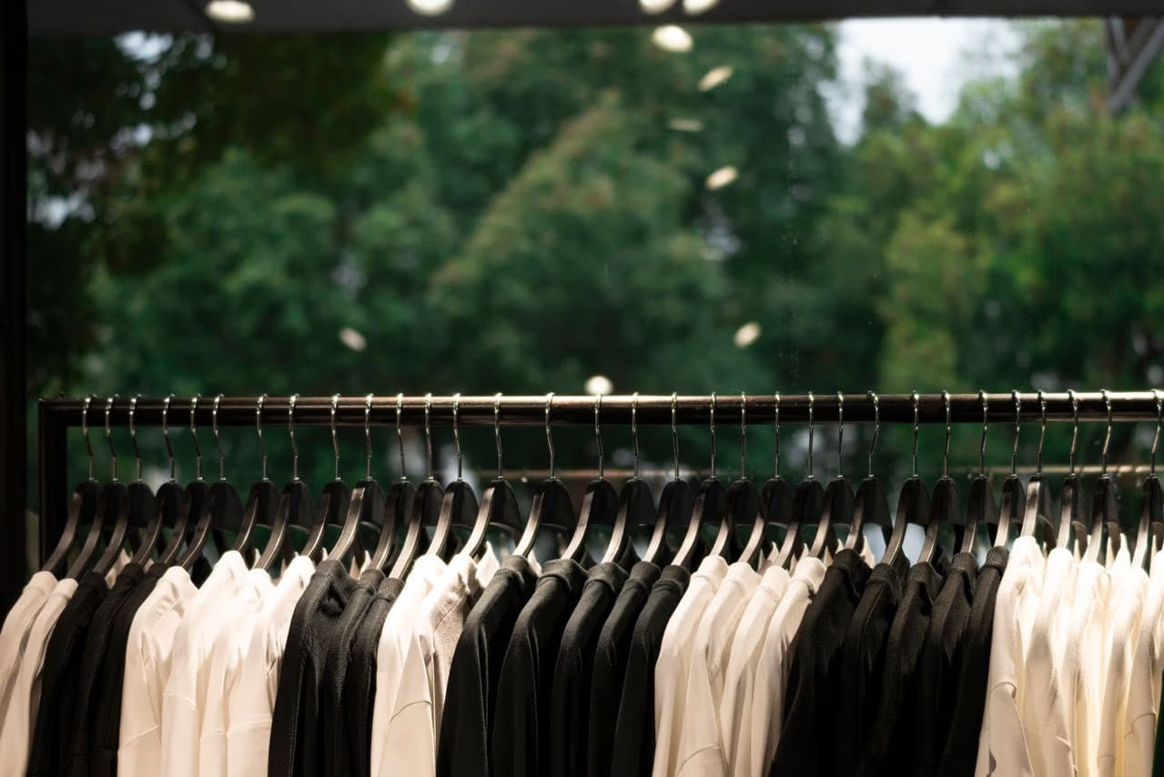 A clothing rack holds a row of black and white shirts against a blurred tree background.