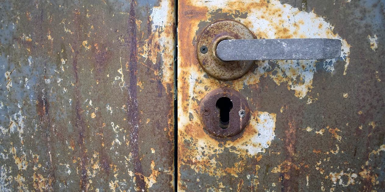 Close-up view of an old rusty metal door with a weathered handle and keyhole.