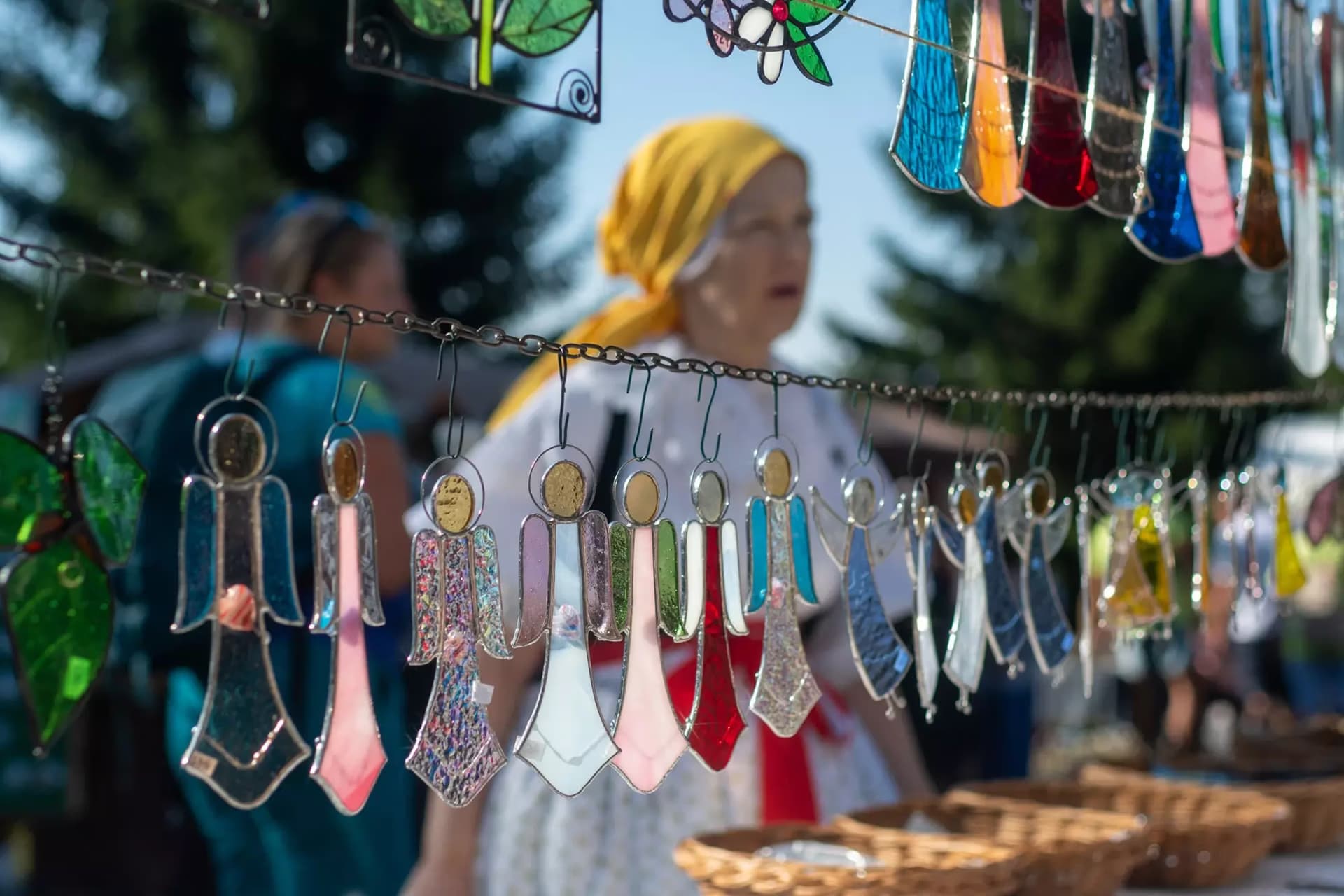 Handcrafted colorful glass angel ornaments hang on a string at an outdoor market stall.