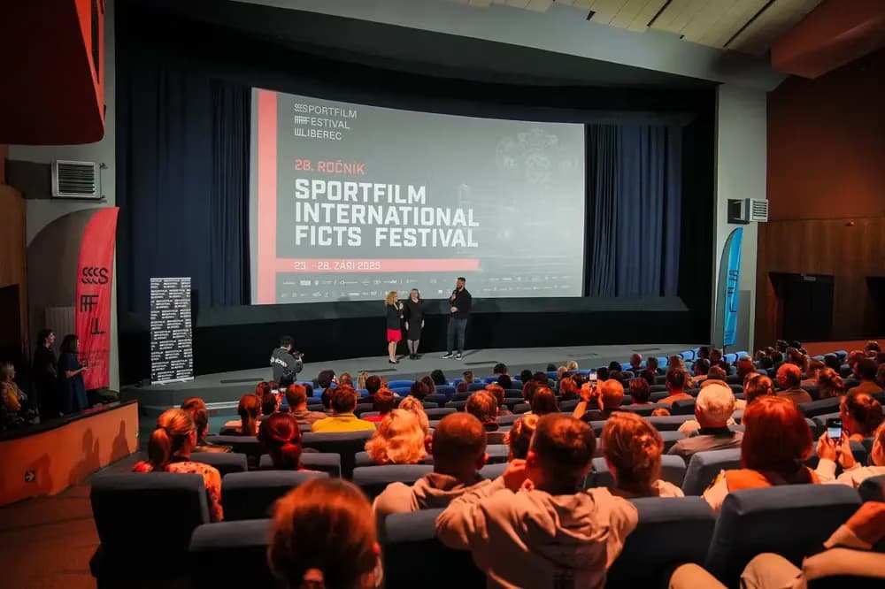 People stand on a cinema stage in front of a screen displaying the Sportfilm International Ficts Festival.