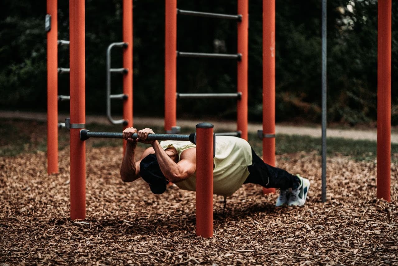 A muscular man performing a push-up exercise on an outdoor calisthenics bar.